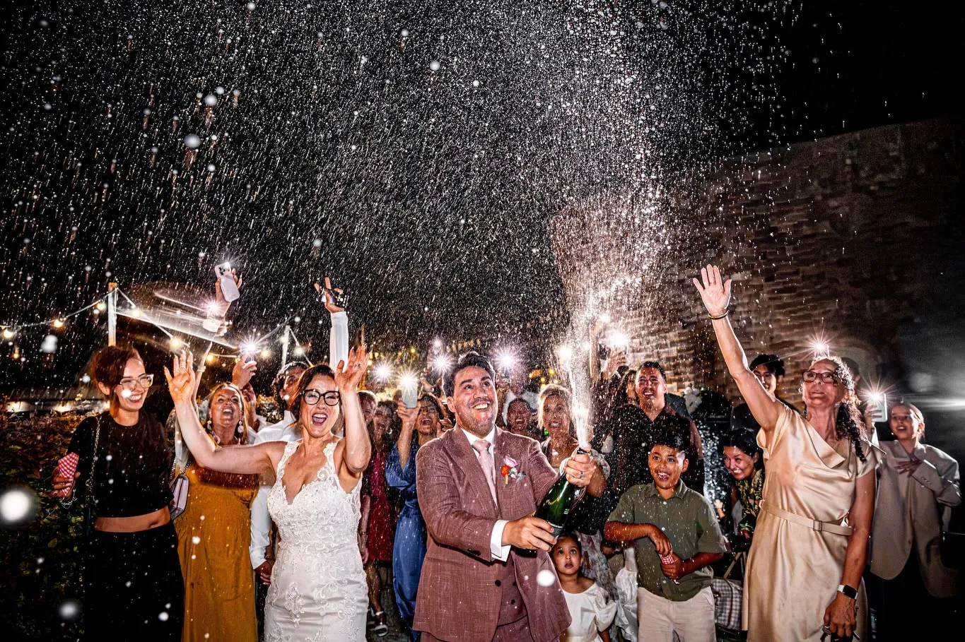 Het bruidspaar juicht met hun gasten tussen sterretjes en champagne in de avond