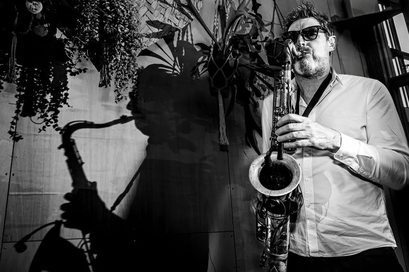 Een saxofonist speelt op het feest, zijn schaduw groot op de muur (zwart-wit)