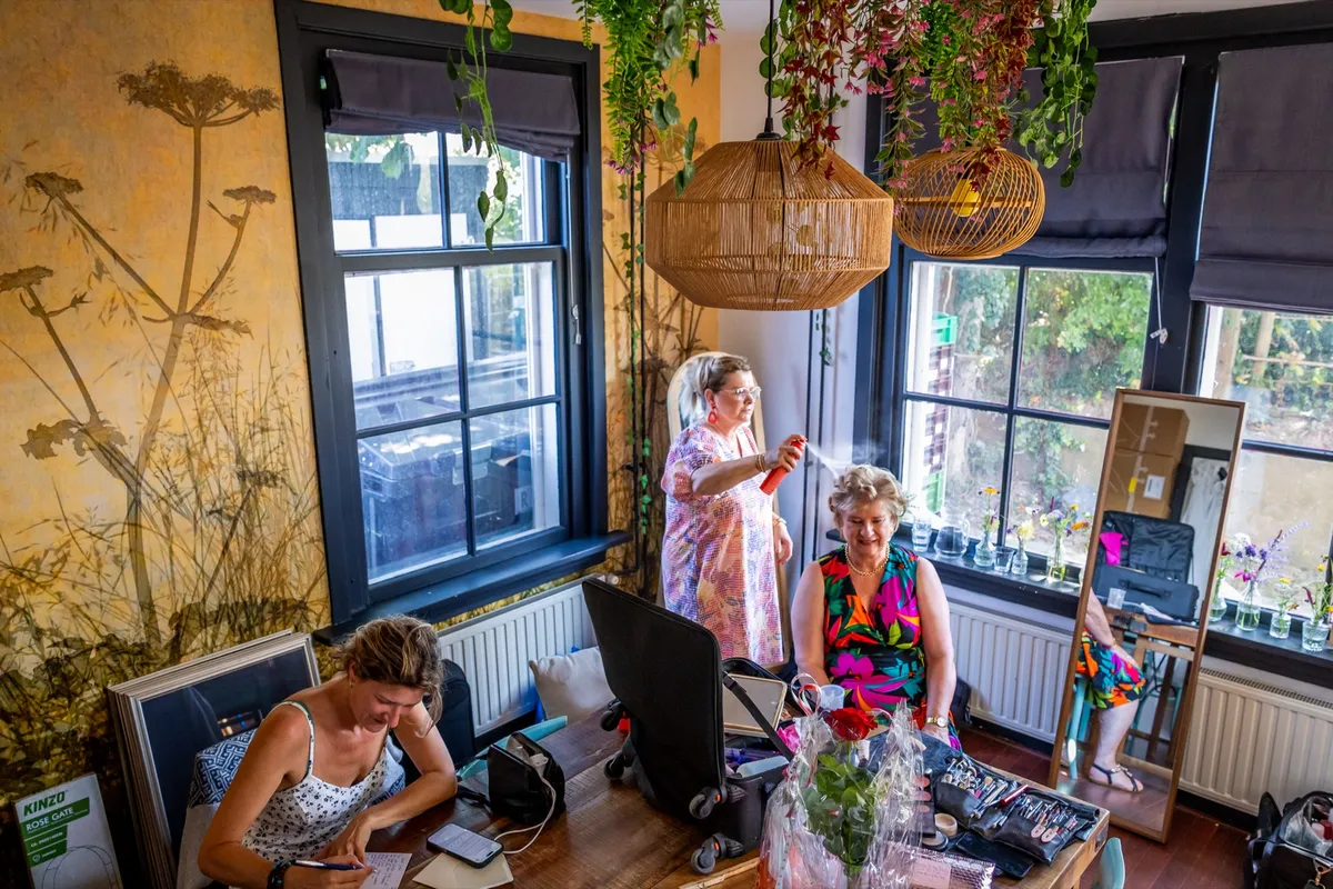 De bruid wordt opgemaakt door de visagiste in een kleurrijke kamer op Tiengemeten