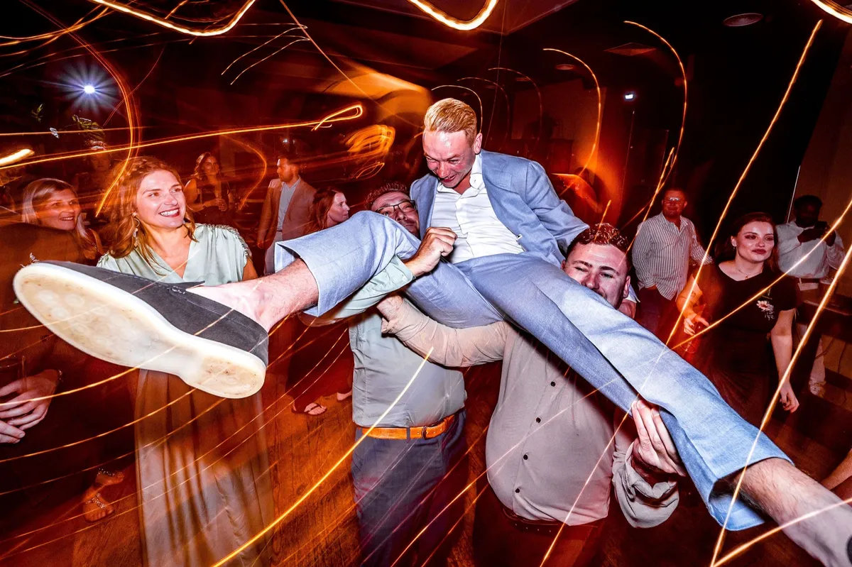 Vrienden gooien de bruidegom de lucht in op het feest, met lichtstrepen van de feestverlichting