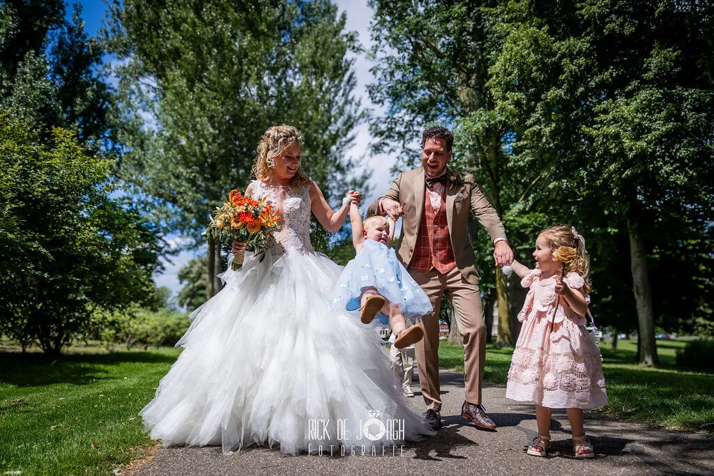 Het bruidspaar wandelt met hun kinderen door het park, de bruid met haar kleurrijke boeket