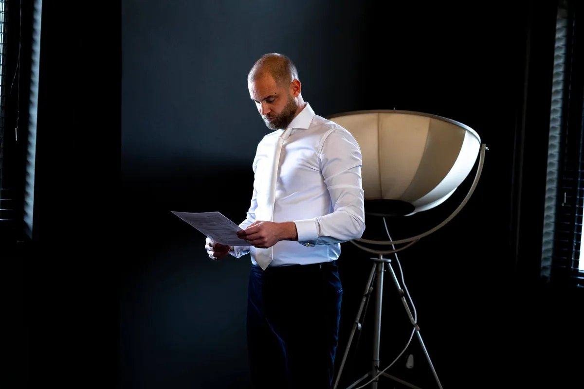 Een man leest zijn tekst nog één keer door in een donkere kamer naast een grote lamp