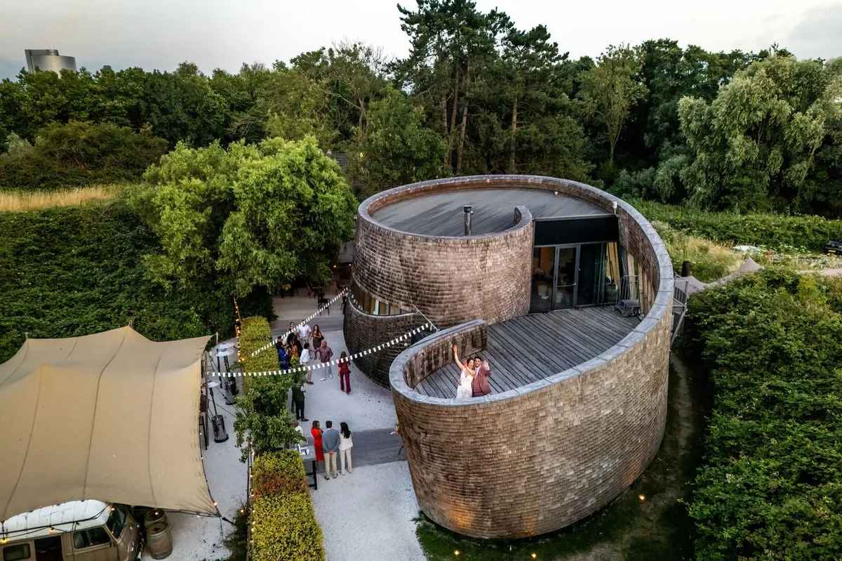 Dronefoto van Paviljoen Puur in Diemen: het ronde paviljoen met houten gevel, de stretchtent en de tuin vol groen