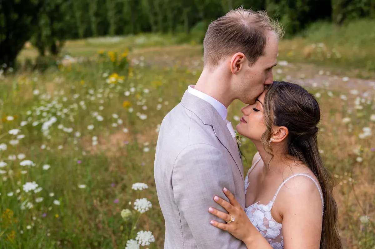 De bruidegom kust de bruid op haar voorhoofd in een veld met bloemen