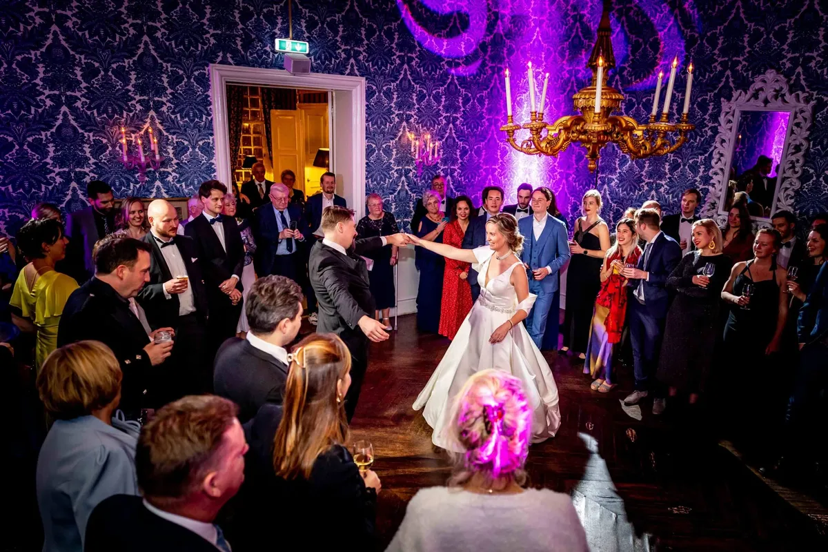 Openingsdans in een zaal met paars licht en kroonluchters, de gasten staan eromheen