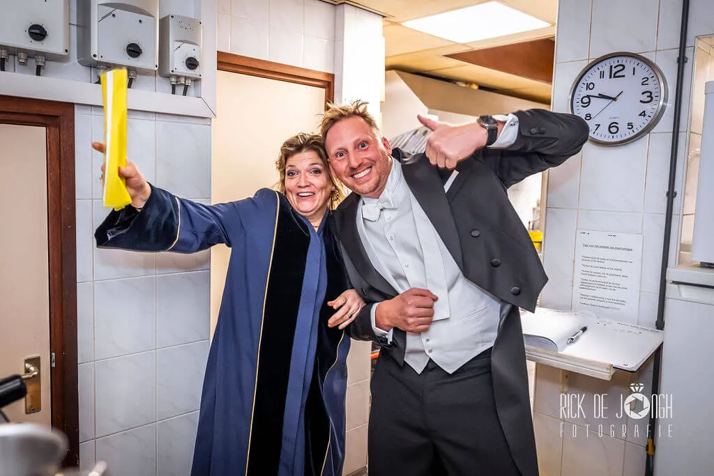 Trouwambtenaar Anke Goedhart en de bruidegom poseren uitgelaten in de gang