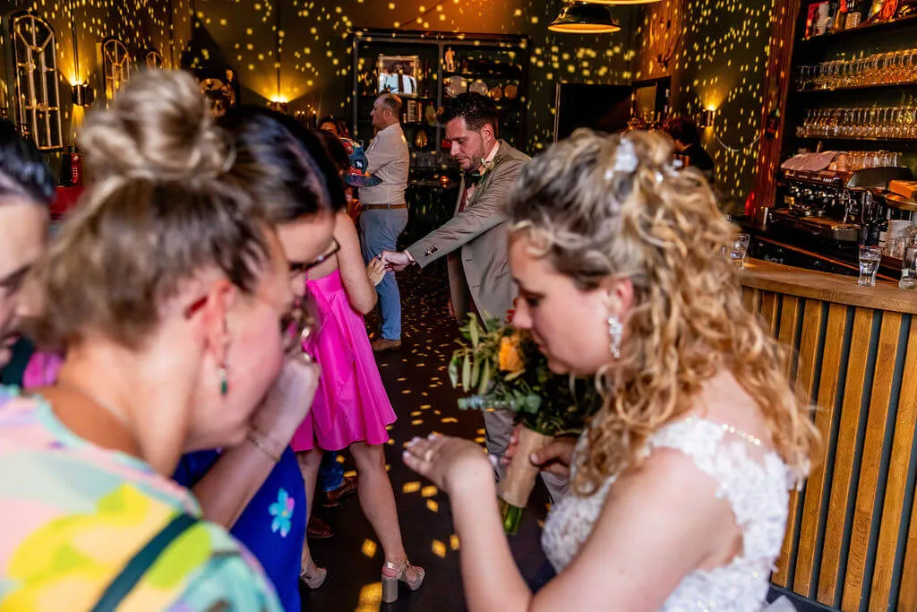 Een gast is ontroerd als de bruid met haar boeket door de sfeervol verlichte bar loopt