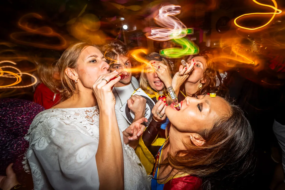 De bruid en haar vriendinnen drinken een shotje Flügel tussen gekleurde lichtsporen op het feest