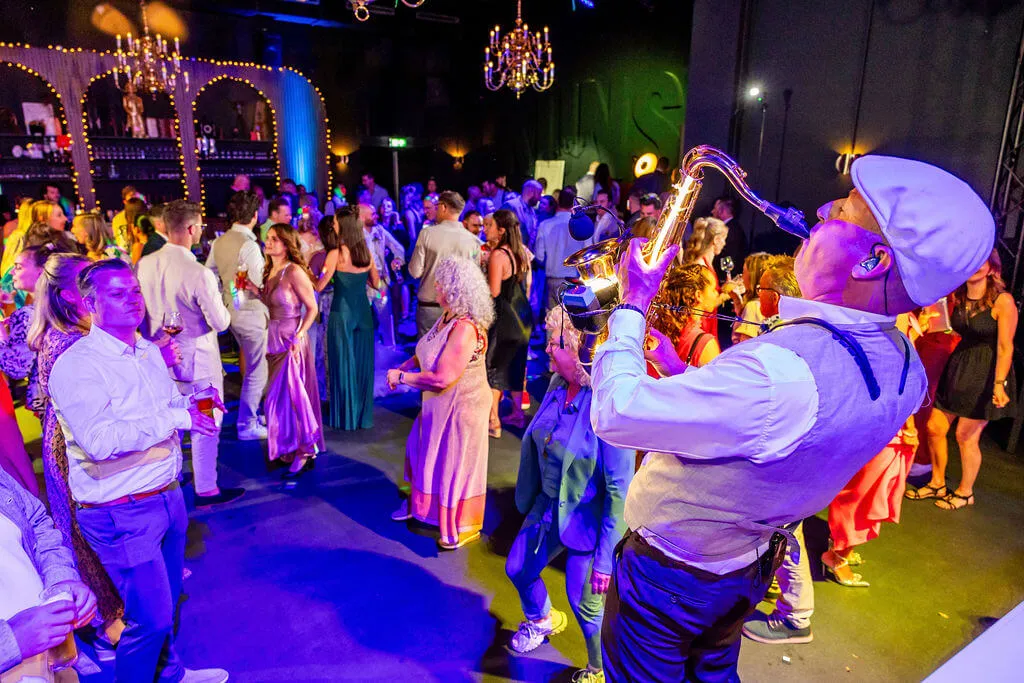 De saxofonist speelt midden tussen de dansende gasten in het gekleurde licht