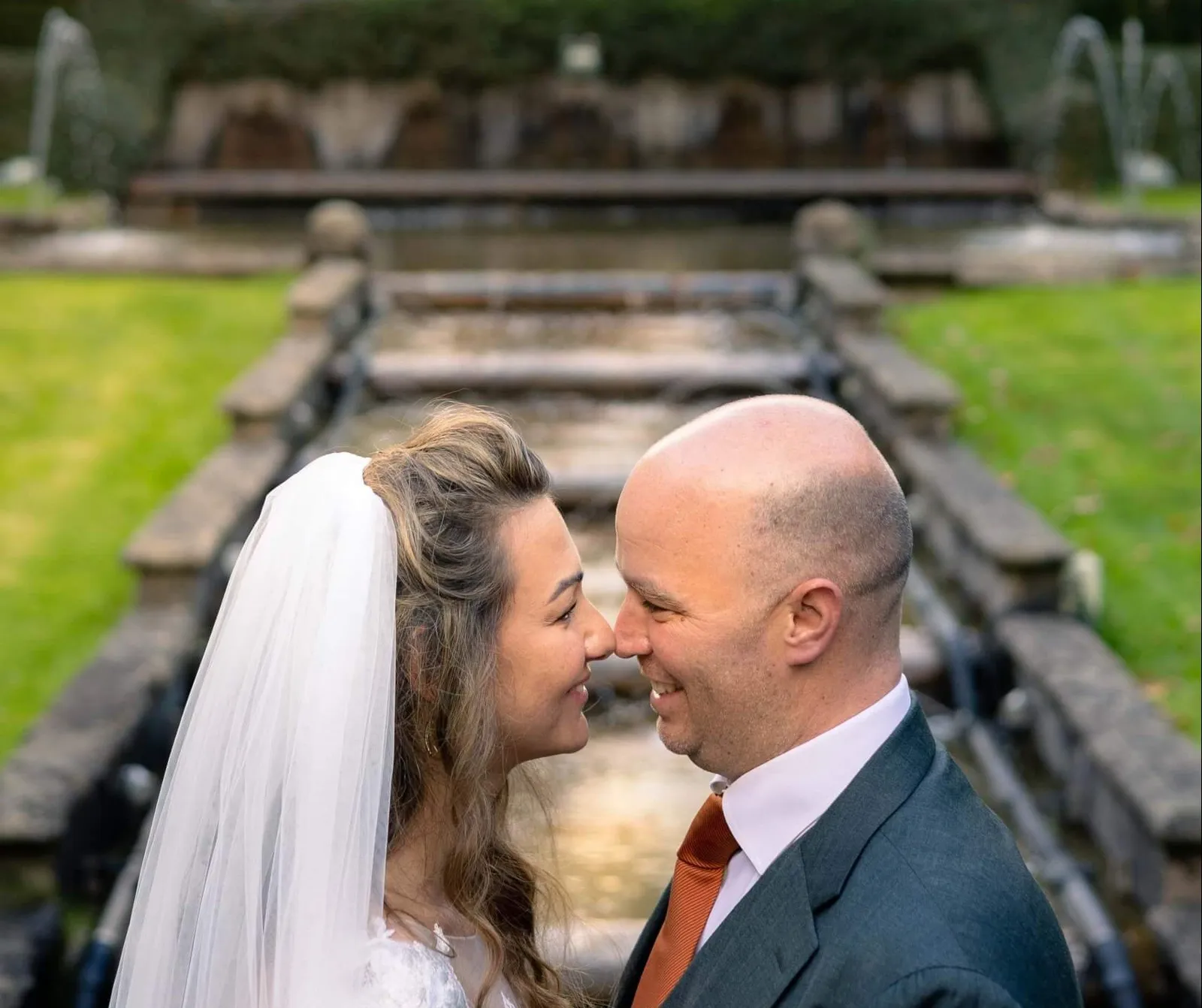 Het bruidspaar staat neus aan neus in de kasteeltuin, met een fontein op de achtergrond