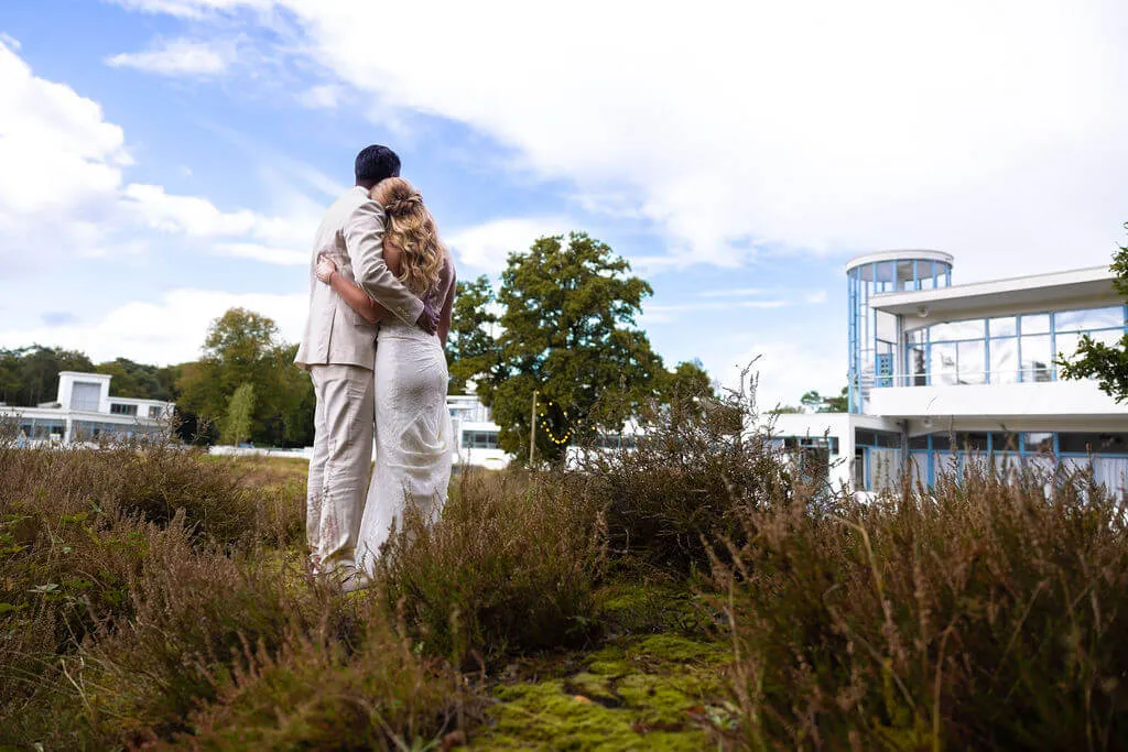 Het bruidspaar kijkt vanaf de heide naar het witte sanatoriumgebouw van Zonnestraal