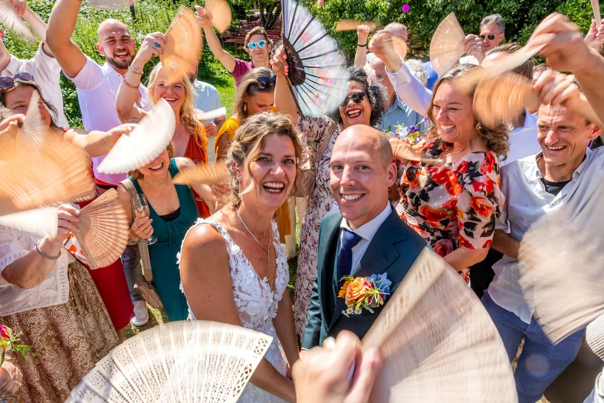Gasten juichen met waaiers rond het pas getrouwde bruidspaar