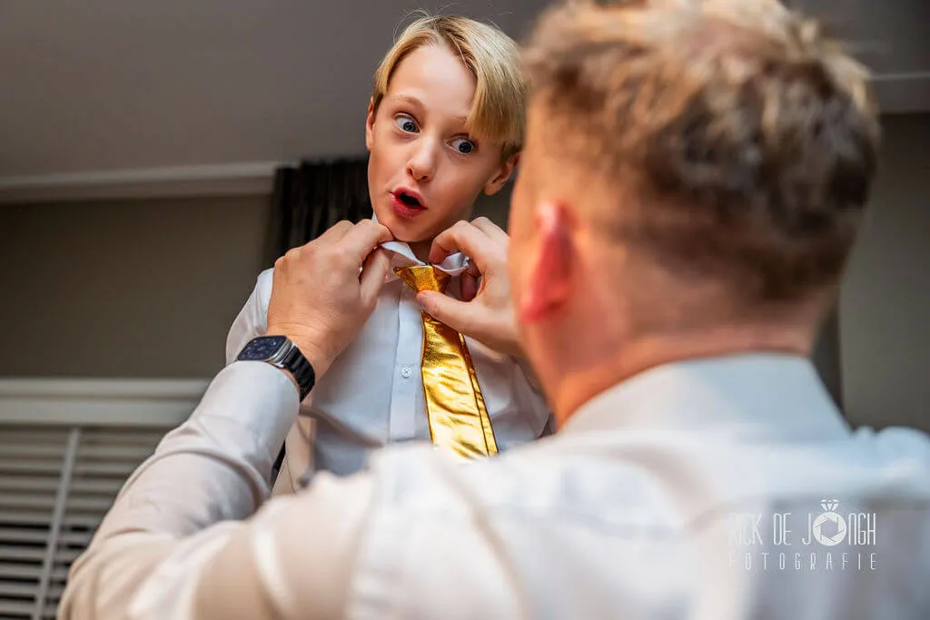 Een jongen trekt een verbaasd gezicht terwijl hij een gouden stropdas omgedaan krijgt