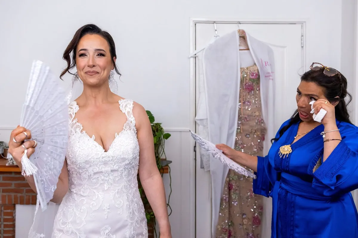 De bruid in haar trouwjurk met een witte waaier, naast haar veegt een vrouw in een blauwe kimono een traan weg