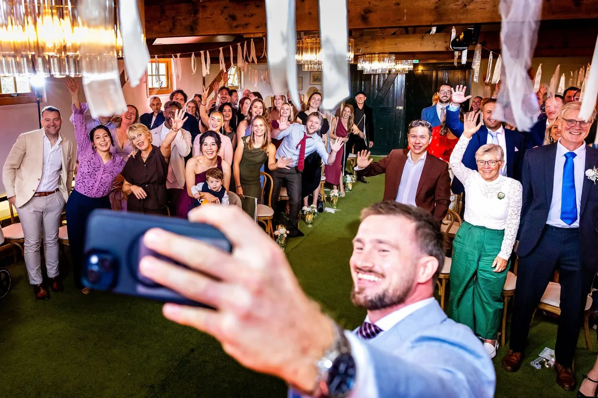 Een gast maakt een selfie met alle zwaaiende en juichende gasten tijdens de ceremonie