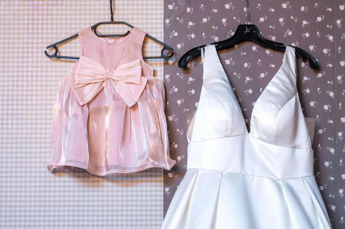 De trouwjurk en het roze jurkje met strik van dochtertje Nora hangen naast elkaar aan de muur