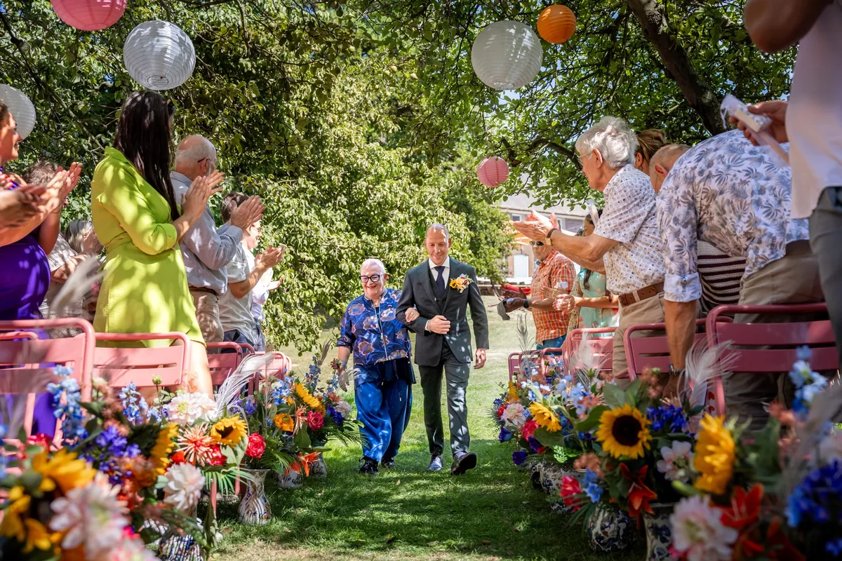 De bruidegom loopt door het gangpad vol bloemen naar de ceremonie