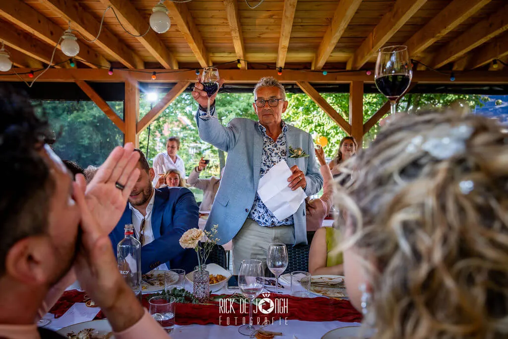 Een gast houdt een speech met het glas geheven, de bruidegom klapt