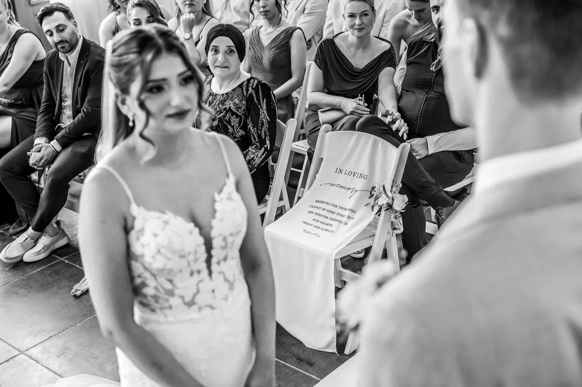 De bruid tijdens de ceremonie, met de gasten op de achtergrond (zwart-wit)
