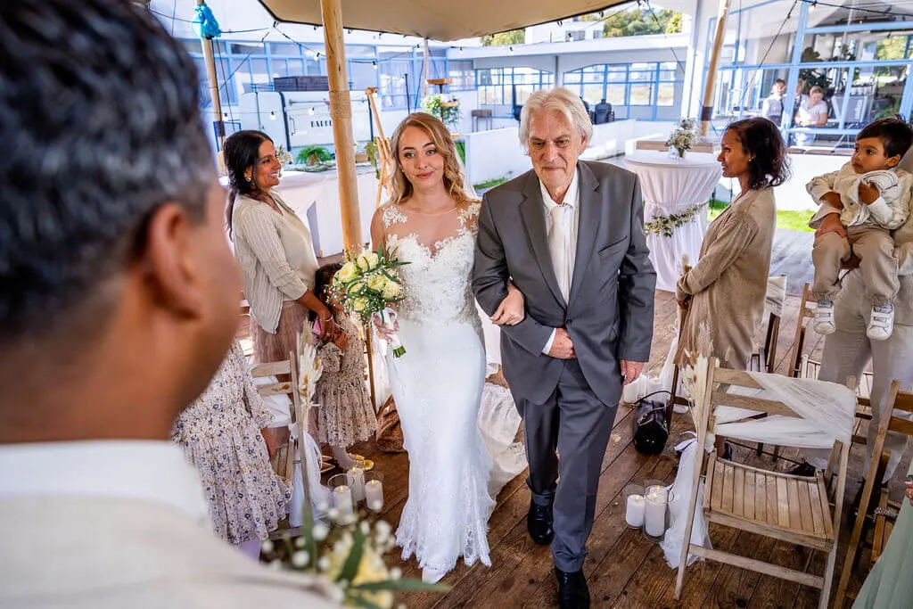 De vader van de bruid loopt met haar naar de ceremonie onder de tent op landgoed Zonnestraal