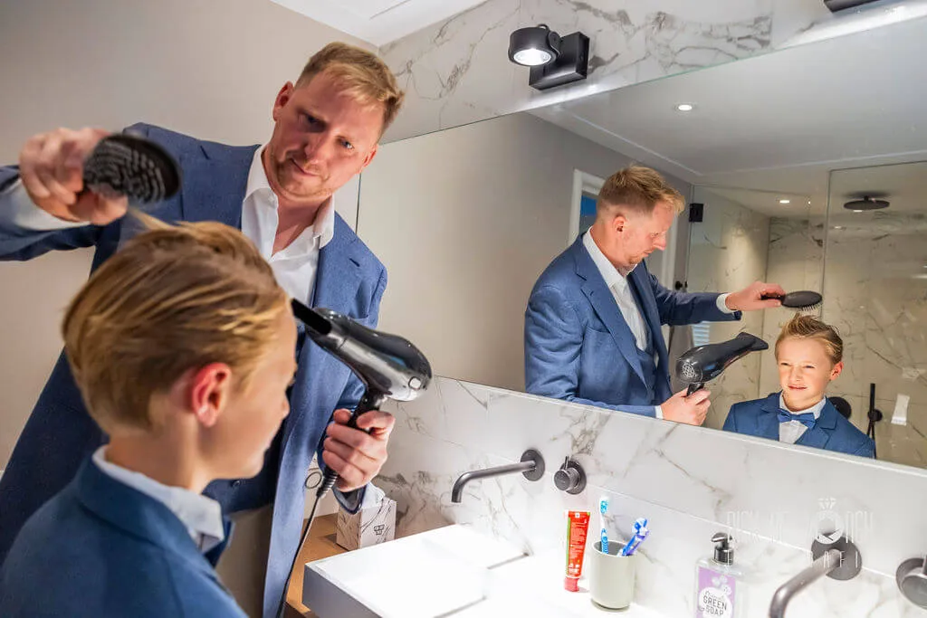 De bruidegom föhnt het haar van een jongen in de badkamer