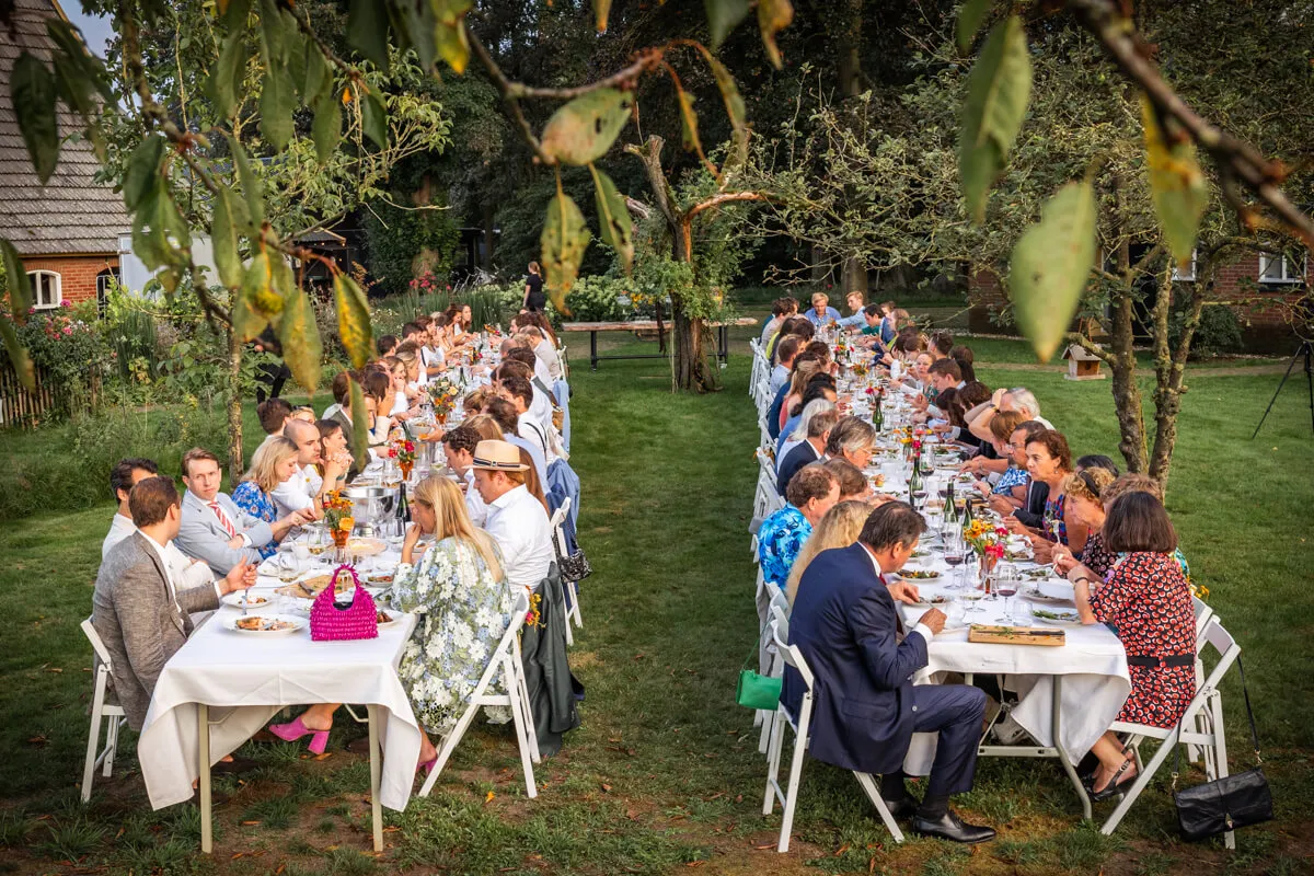 Lange gedekte tafels met gasten in een groene tuin tijdens het trouwdiner