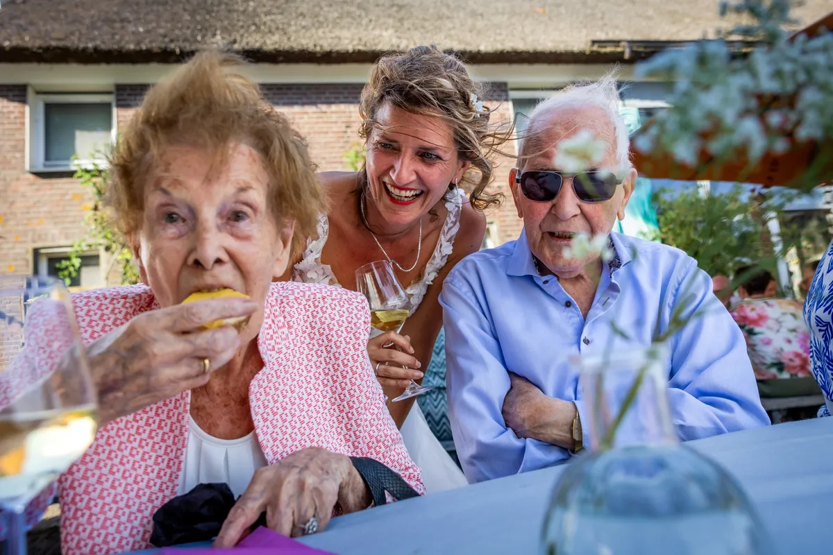 Een oudere gast smult van het eten terwijl de bruid lachend toekijkt