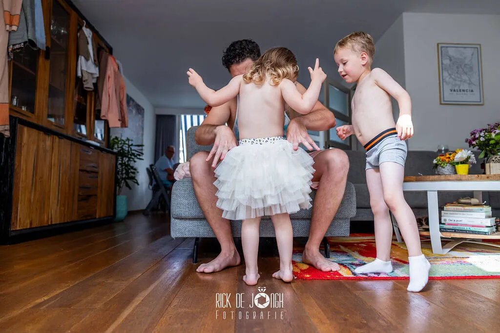 Thuis worden de kinderen aangekleed, een jongetje springt in zijn onderbroek door de woonkamer