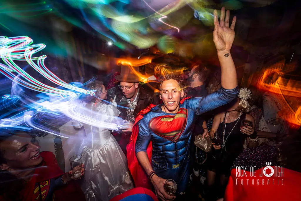 Een gast verkleed als Superman danst tussen kleurige lichtsporen
