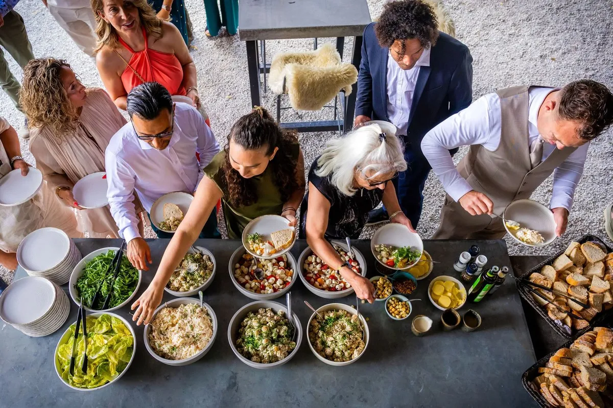 Gasten scheppen op van een kleurrijk buffet met salades en brood, van bovenaf gefotografeerd