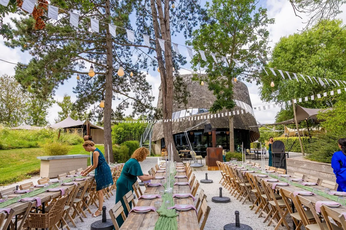 Lange gedekte tafels in de tuin van Paviljoen Puur, met slingers tussen de hoge dennen